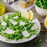 Rocket salad with Parmesan cheese, lemon, olive oil and seasonings on wooden background